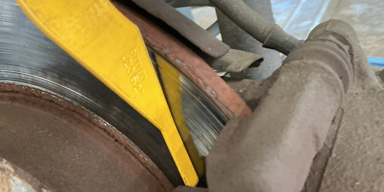 brake-pad-thickness-gauge-check-rear-caliper.jpg Yellow brake pad thickness gauge being used to measure remaining friction material on a rear brake pad