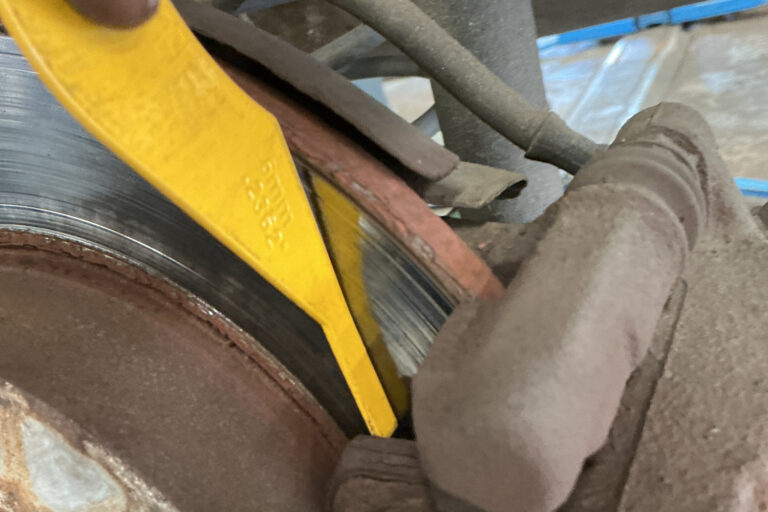 brake-pad-thickness-gauge-check-rear-caliper.jpg Yellow brake pad thickness gauge being used to measure remaining friction material on a rear brake pad