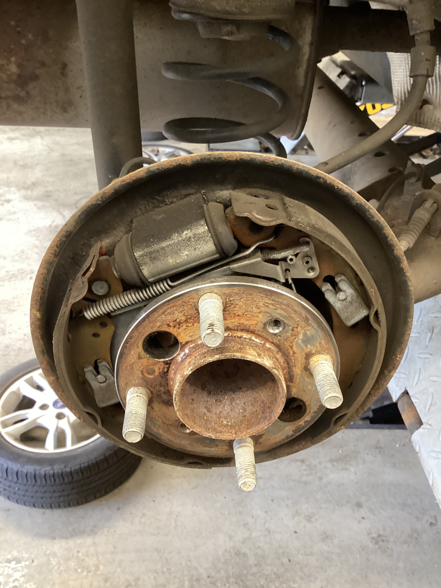 Rear drum brake with the drum removed showing rusty brake shoes, springs and handbrake lever mechanism
