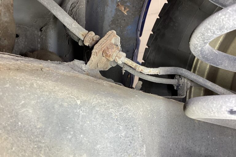 Corroded brake pipe union at the flexible hose bracket on a car's rear suspension