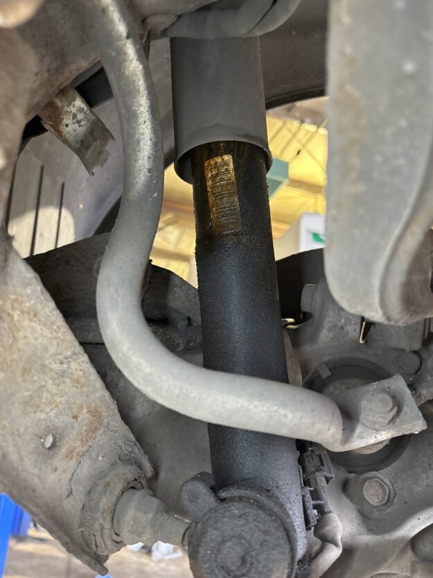 Rear shock absorber with wet oil visible on the exposed damper rod below the dust cover