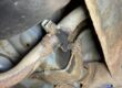 Corroded exhaust joint and clamp under a car on a ramp in a Lindleys workshop