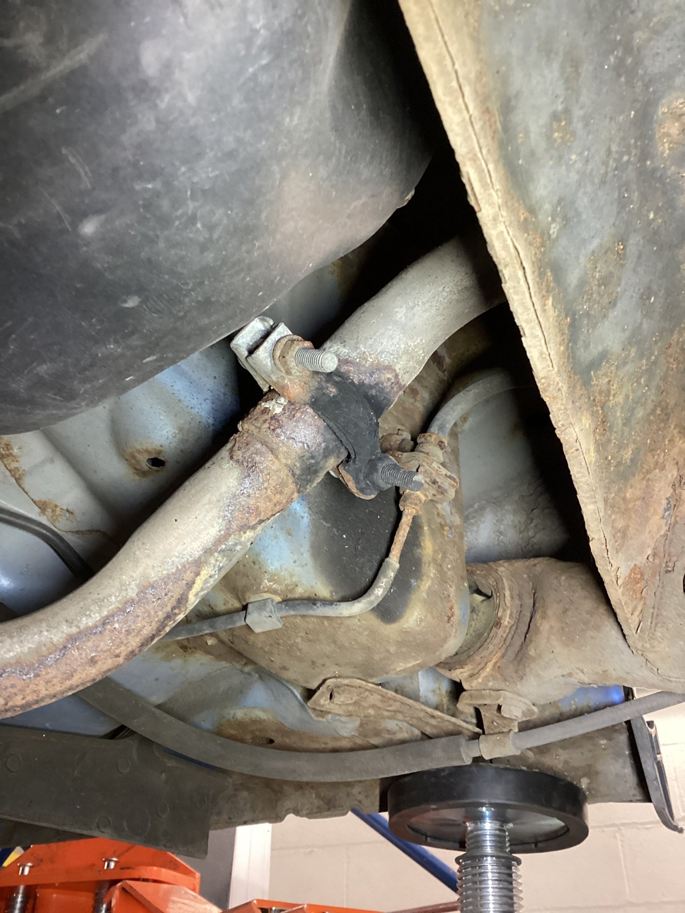 Corroded exhaust joint and clamp under a car on a ramp in a Lindleys workshop