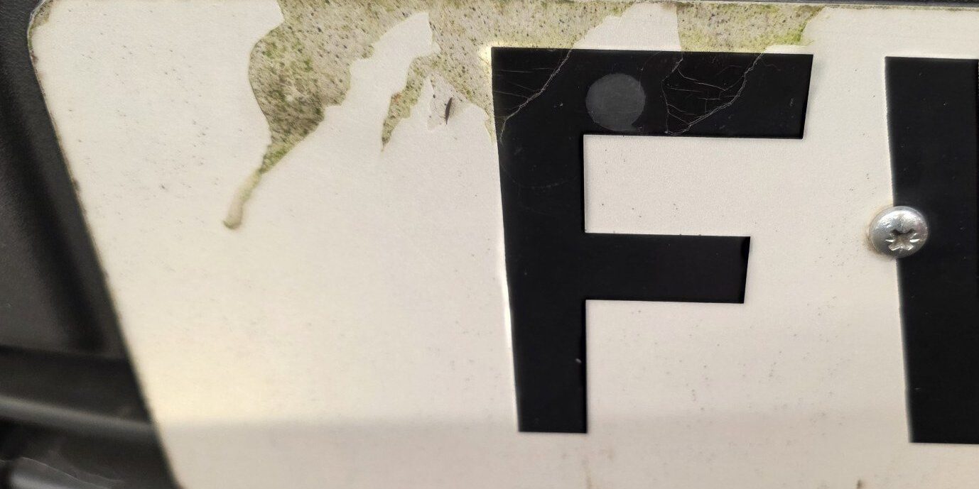number-plate-delaminating-peeling-screw Number plate peeling at the top edge with a fixing screw through a character