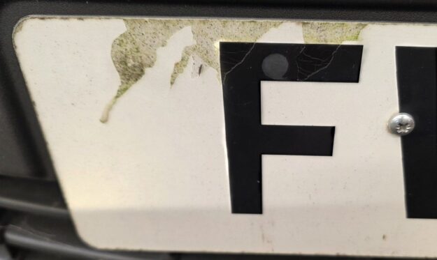 Number plate peeling at the top edge with a fixing screw through a character