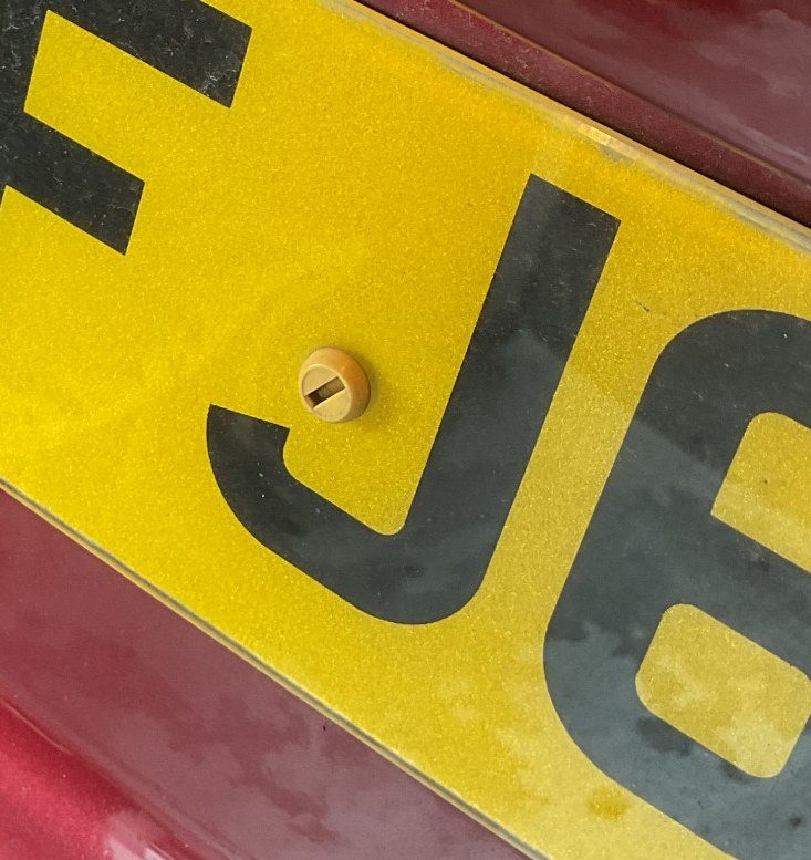 Yellow rear number plate with a fixing cap placed inside a character