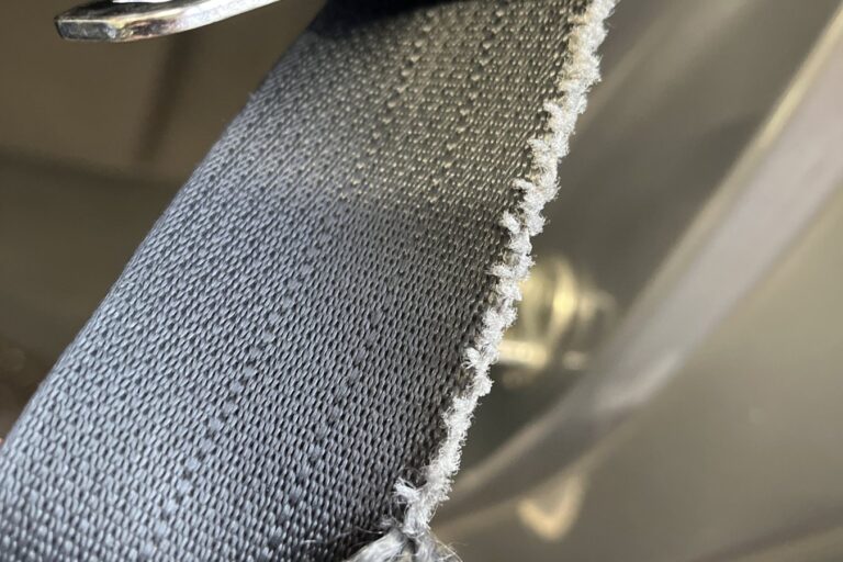seat-belt-frayed-cut-edge-mot-fail Seat belt webbing with a frayed, cut edge beside the buckle tongue
