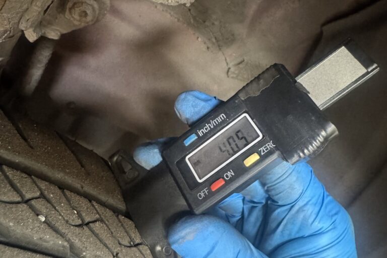 Technician checking front tyre tread depth with a digital gauge during a tyre inspection