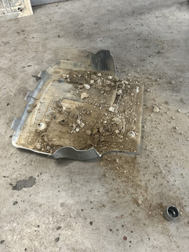 Car engine undertray removed in a workshop, full of gravel and soil