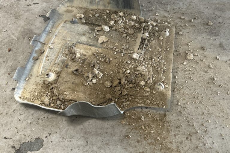 undertray-full-of-gravel-removed Car engine undertray removed in a workshop, full of gravel and soil